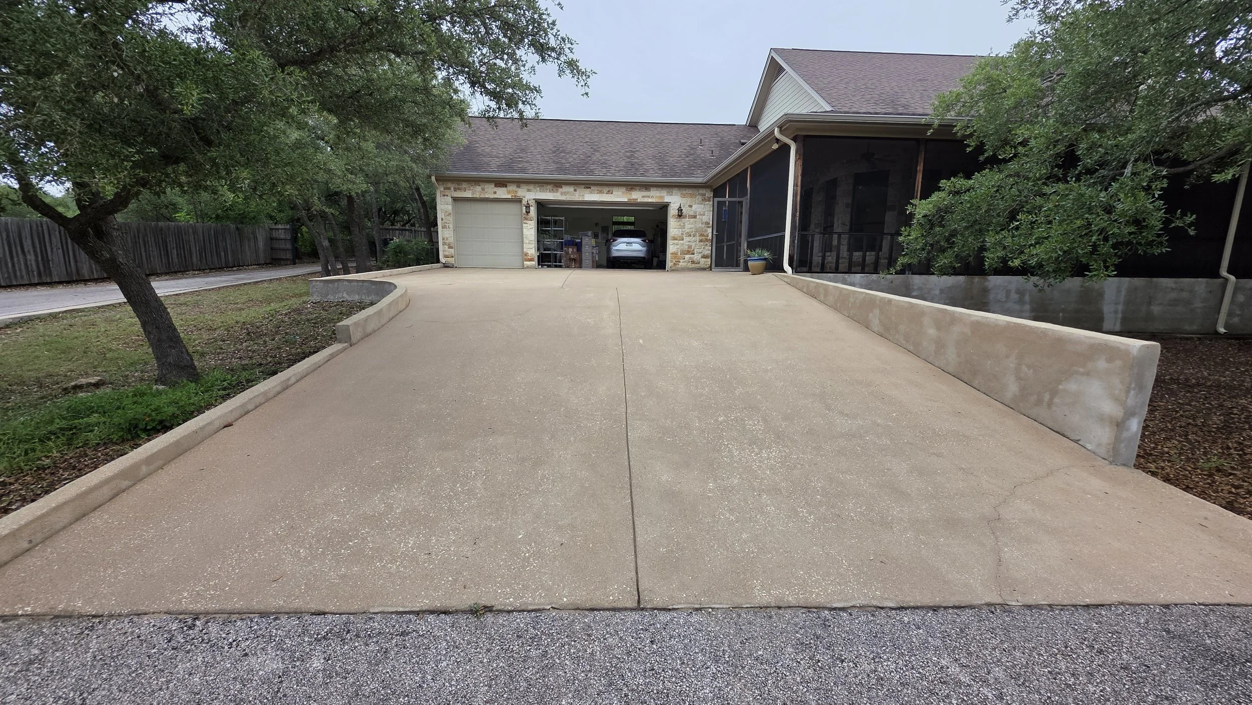 Front view of a house with a driveway, garage, trees, and a screened porch.