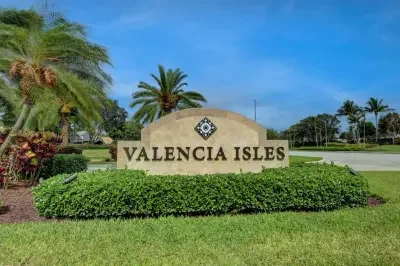 Sign reading 'Valencia Isles' in front of lush green grass and palm trees under a blue sky.