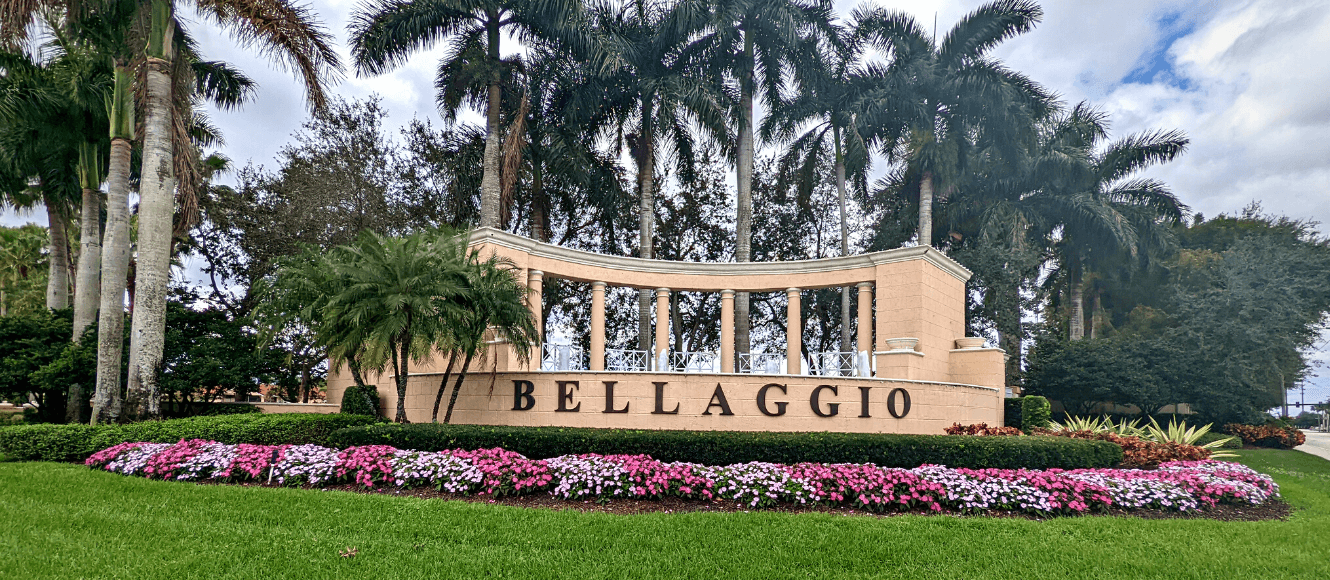 Sign with the word 'BELLAGGIO' in front of a landscaped area with pink and purple flowers, green shrubs, palm trees, and a cloudy sky.
