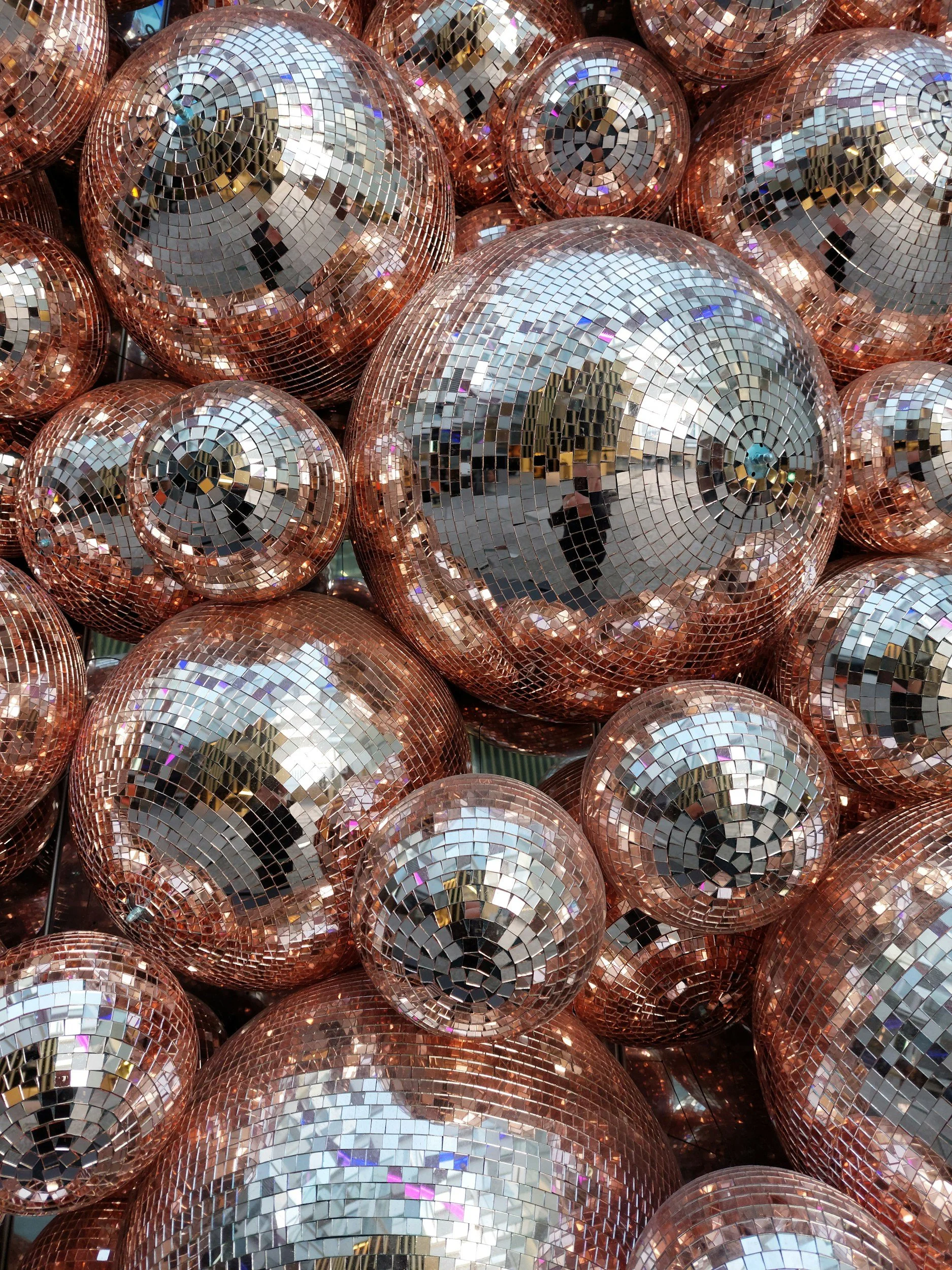 Close-up view of multiple disco balls with reflective mirrored surfaces, showing a mosaic of small square mirrors creating a shiny, sparkling effect.