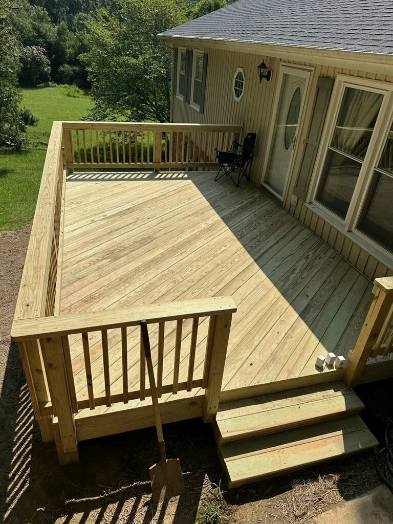 Wooden backyard deck attached to house with sliding glass door, small steps, and outdoor chair, overlooking green lawn and trees.