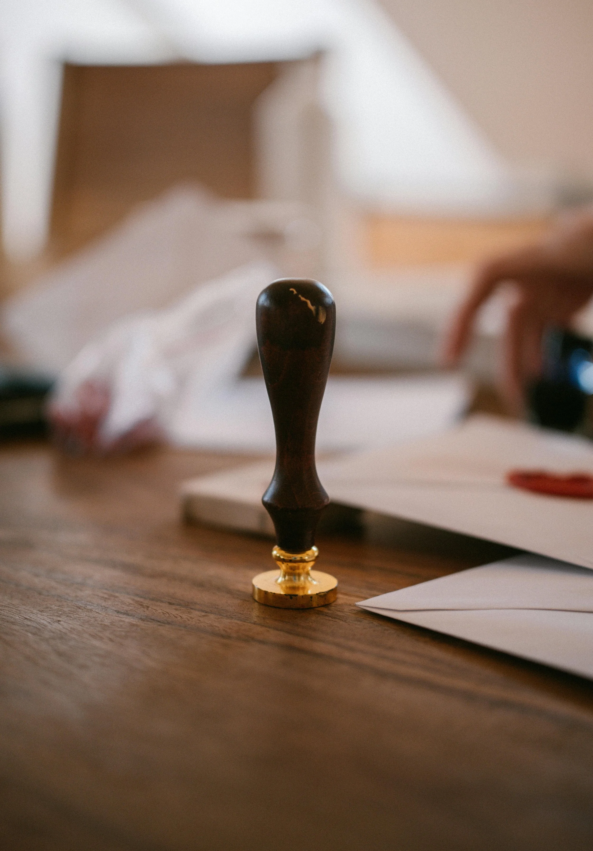 Close-up of a wooden stamp with a black rubber surface on a wooden table with scattered papers and a blurred background.