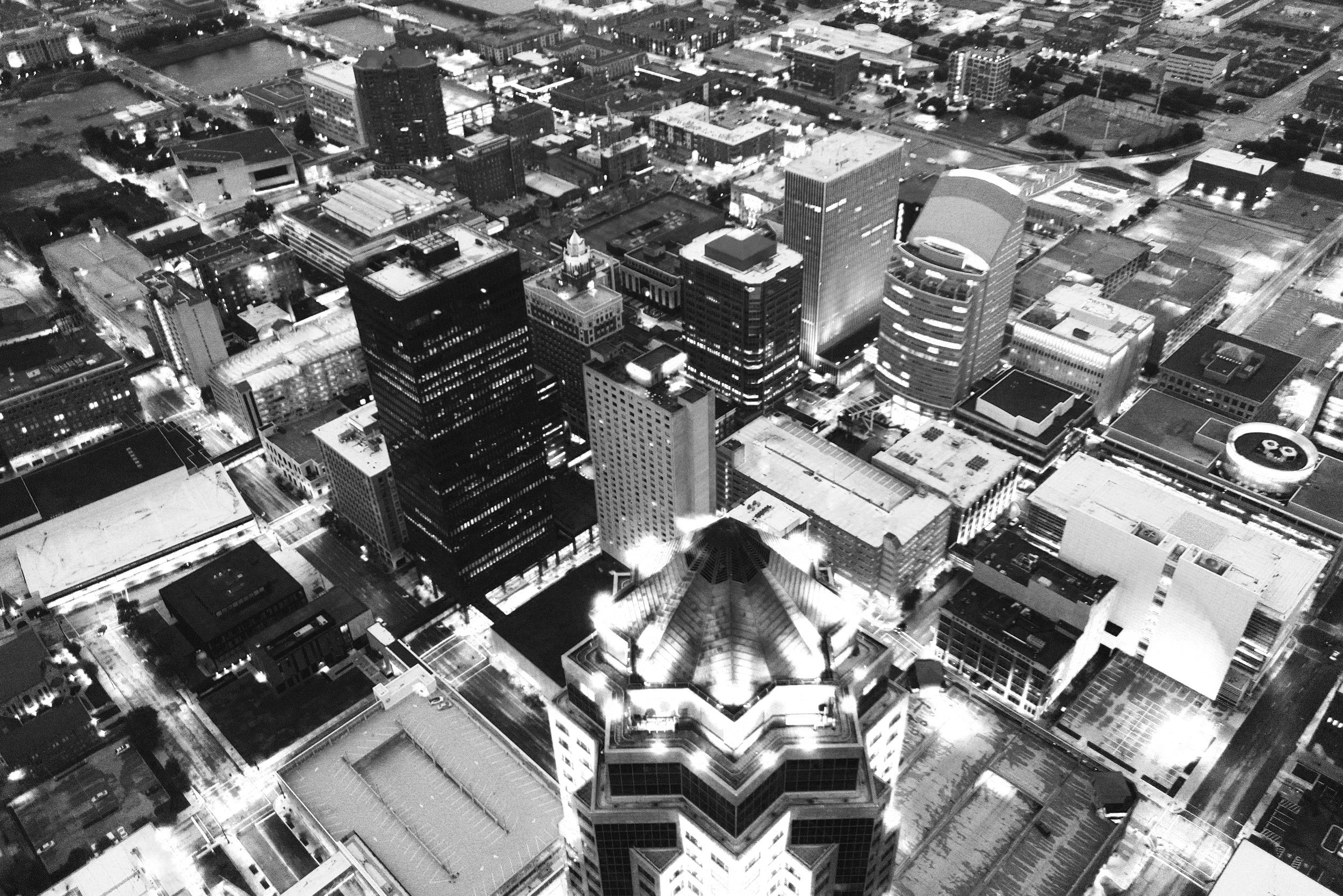 Nighttime aerial view of a cityscape with tall skyscrapers, illuminated streets, and surrounding shorter buildings.