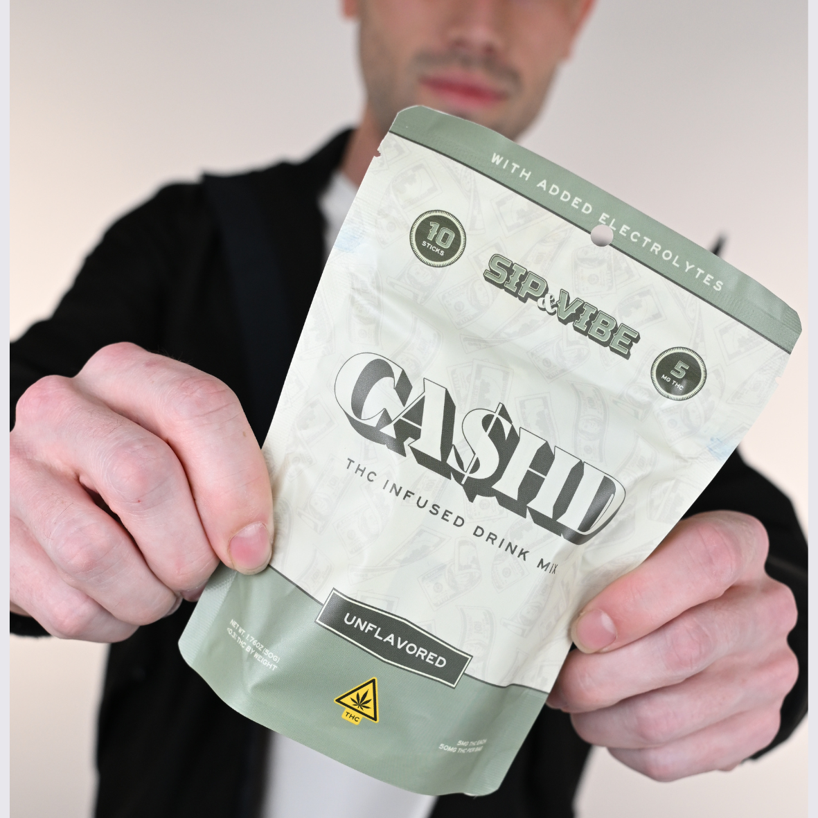 A man holding a cannabis-infused drink package labeled 'GASHED' with THC warning symbols and flavor 'unflavored'.