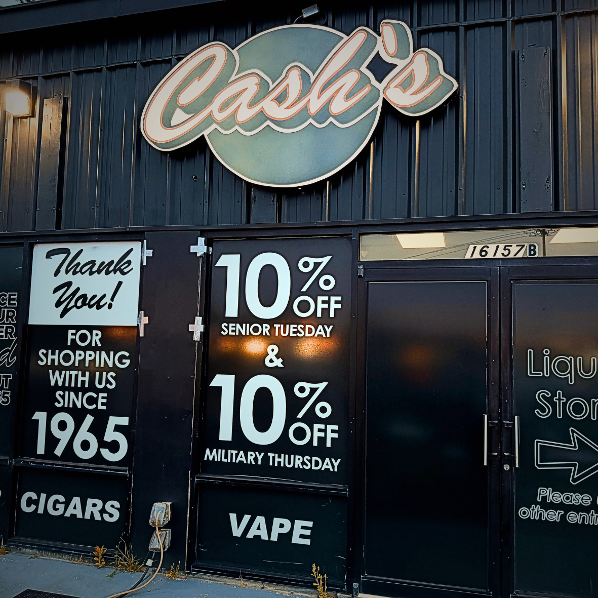 Storefront with a large sign reading 'Cash's'. Posters advertising 10% discounts for senior Tuesday and military Thursday, and signs mentioning cigars and vape, with the store's address 16157B.