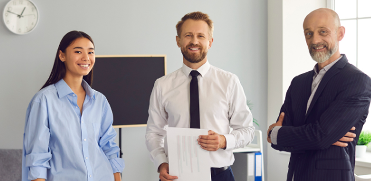 Three professionals standing together in an office, smiling at the camera.