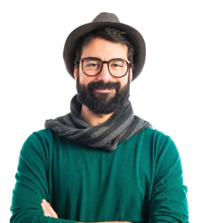 A man with a beard, glasses, and a hat, wearing a green sweater and a scarf, smiling with arms crossed.