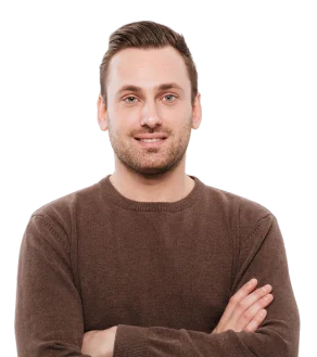 A young man with short brown hair and a beard, wearing a brown sweater, smiling with arms crossed against a white background.