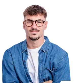 Portrait of a young man with glasses and facial hair, wearing a denim jacket over a white shirt, against a plain white background.