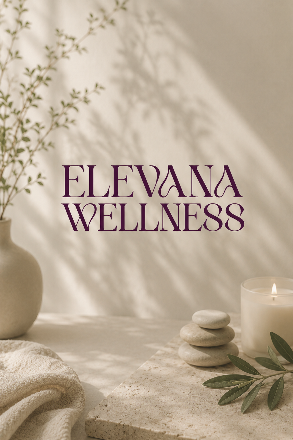 A sign reading 'Elevana Wellness' in purple font on a cream-colored wall. The scene features a beige vase with green leafy branches, a lit white candle, a stack of smooth white stones, and some green leaves on a light-colored marble surface. Shadows of the branches are softly cast on the wall.