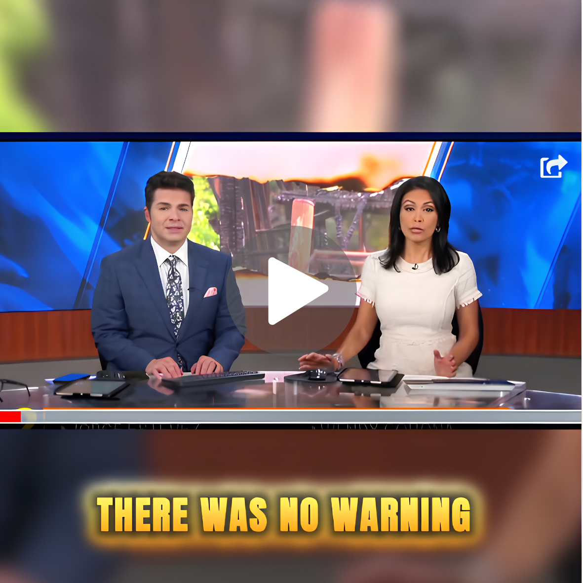 News anchors reporting in a studio with a large screen behind them showing an image of a burning building or vehicle.