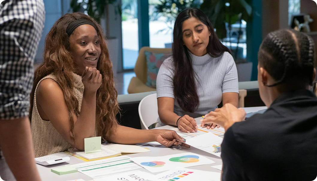 Women engaged in a business meeting, discussing papers with colorful charts and graphs, in a modern office setting.
