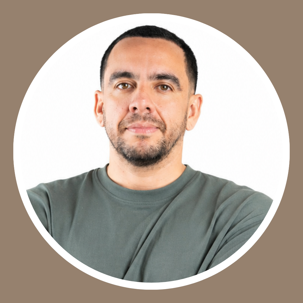A man with short dark hair and a beard, wearing a green T-shirt, taking a selfie against a white background.