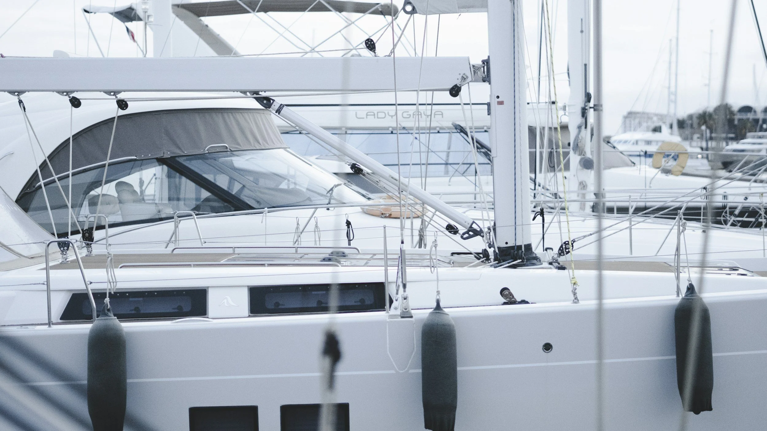 Close-up of a white sailboat docked at a marina with multiple yachts in the background.
