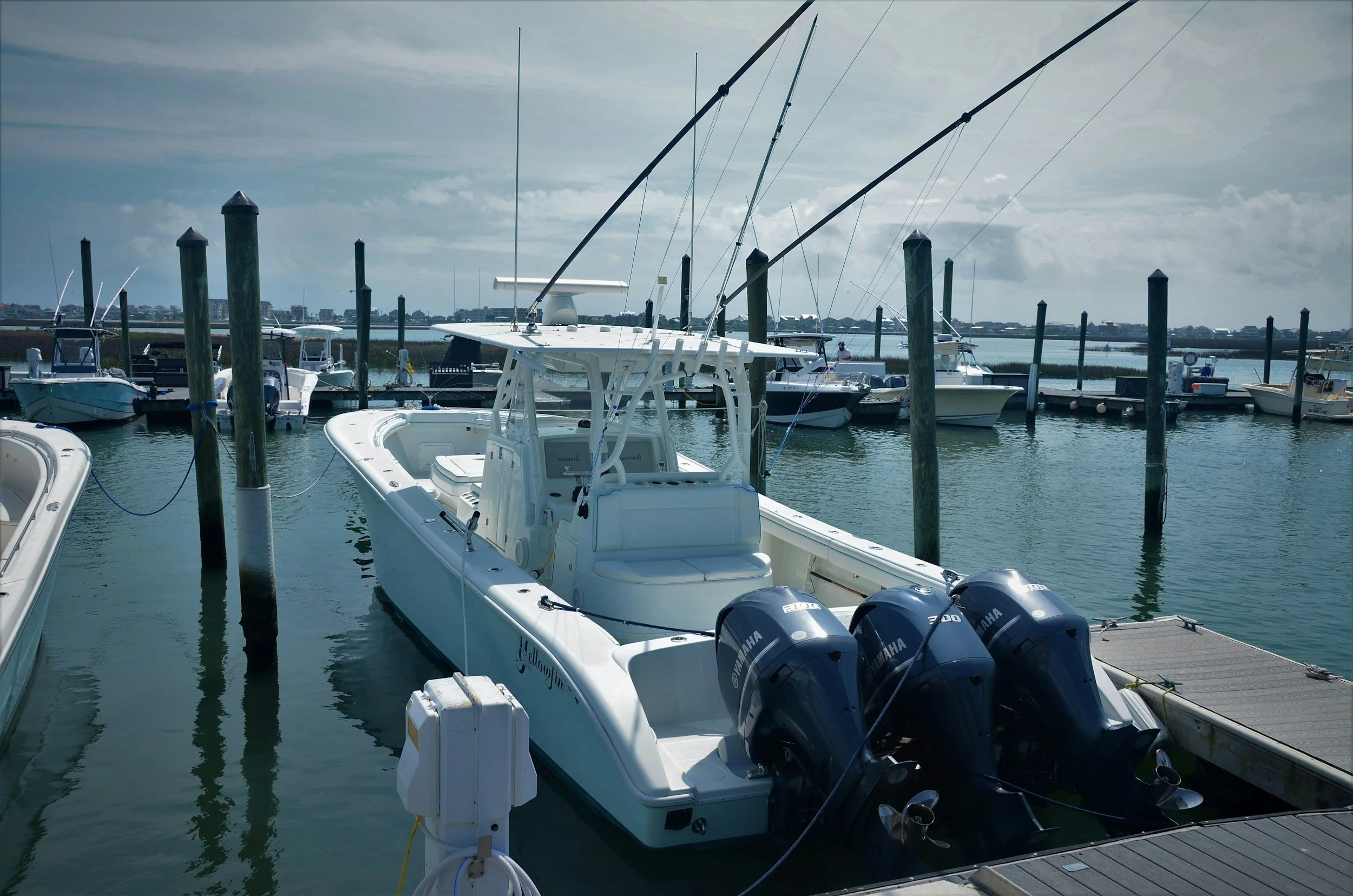A marina with sailboats and motorboats docked, some at a pier, under a cloudy sky.