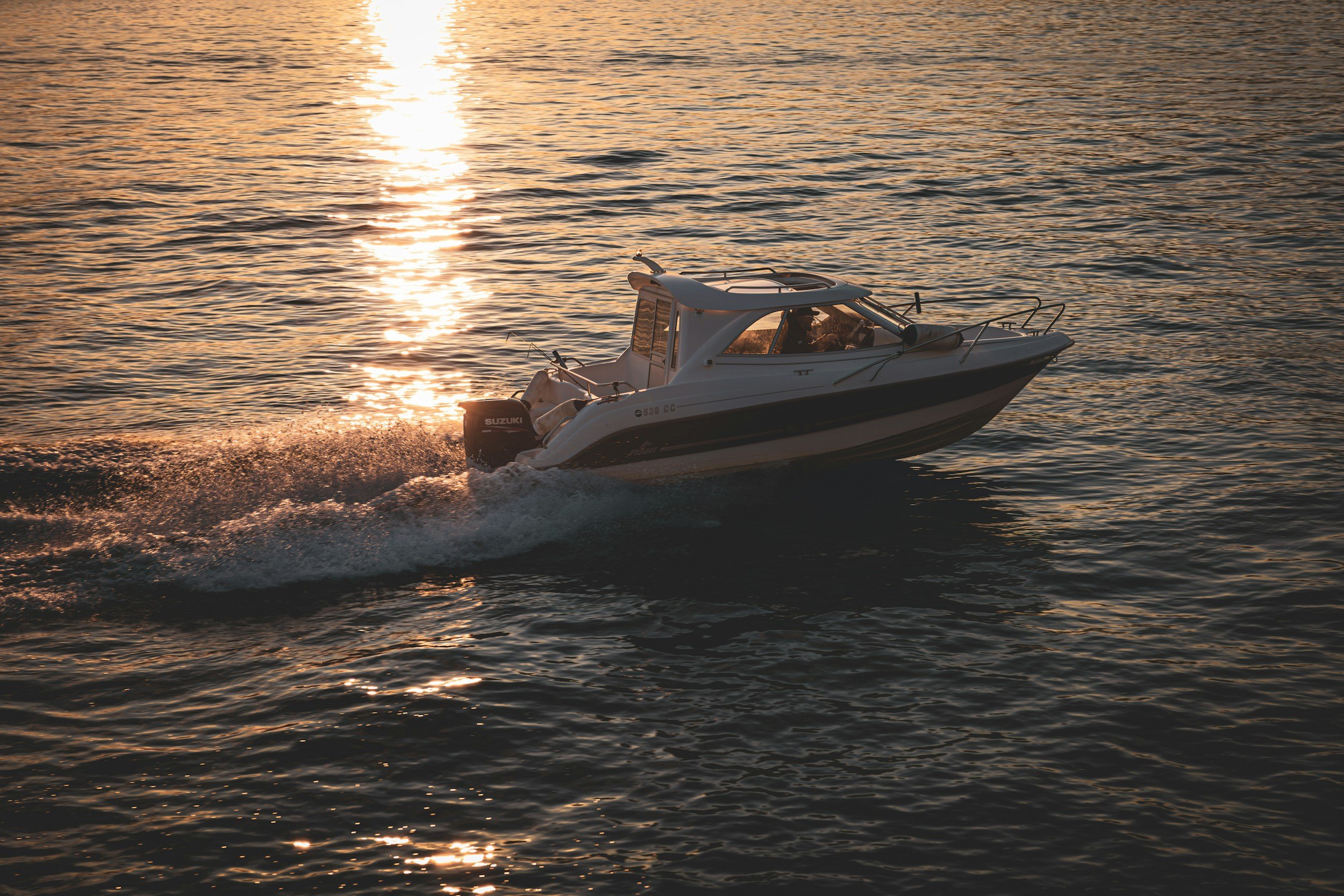 A white motorboat speeding on the water during sunset, creating a splash behind it with the sun reflecting on the water.