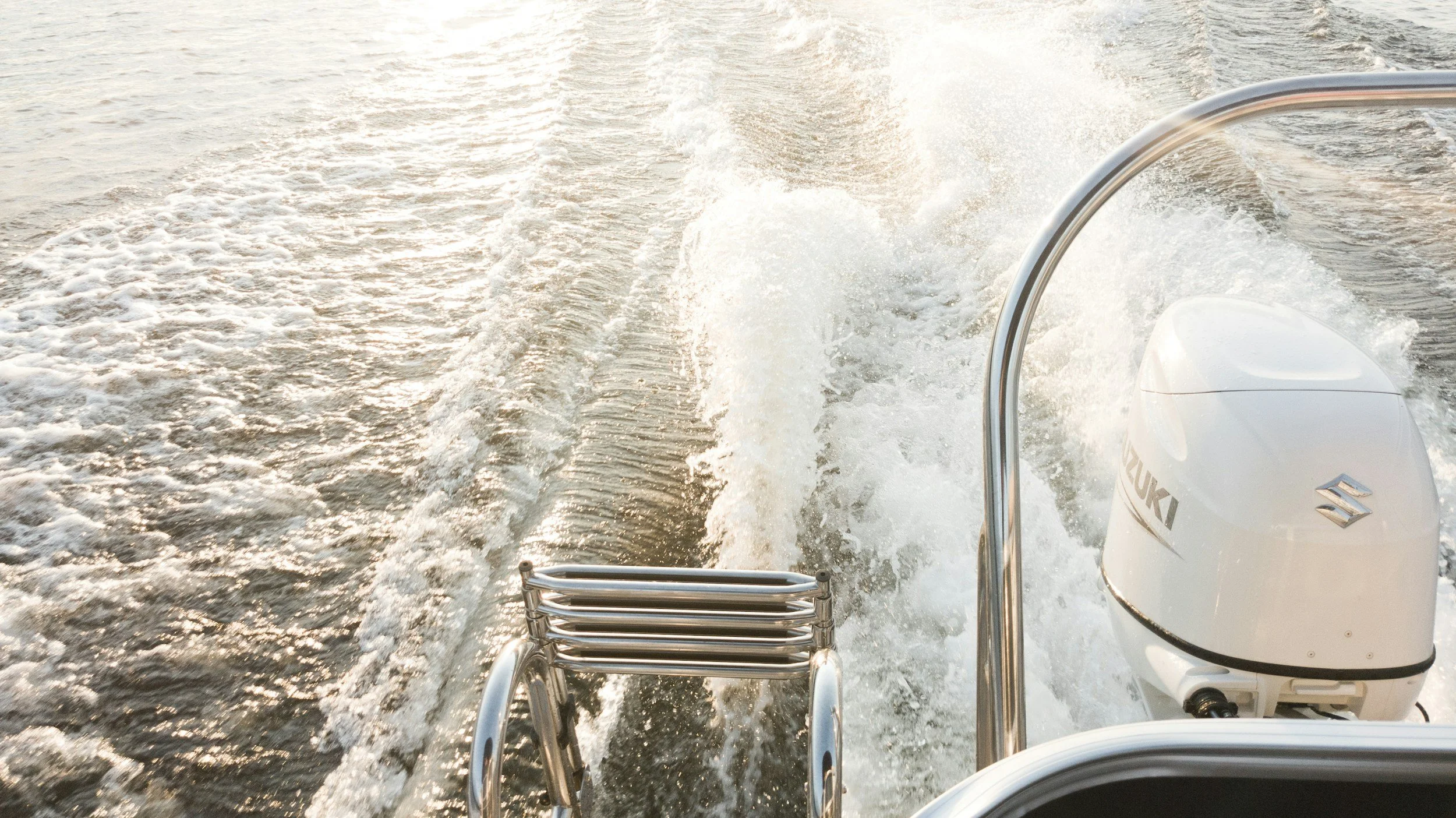 The photo shows the back of a boat speed motor engine with water splashing behind it as the boat moves forward on the water, during sunset.