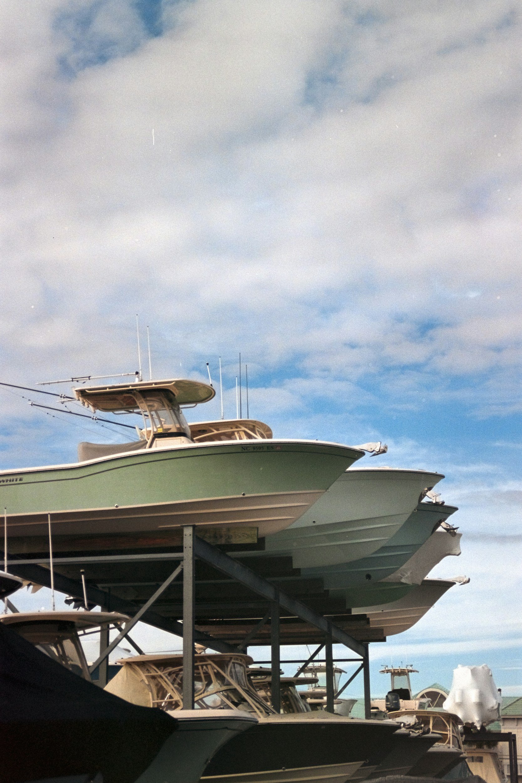 Multiple boats stacked on display at a marina, with a partly cloudy sky in the background.