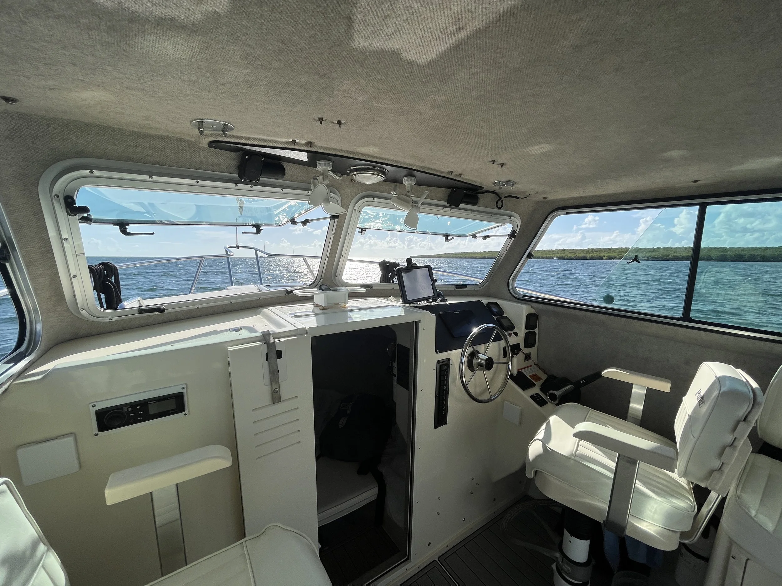 Interior of a boat cockpit with windows showing water and sky outside, featuring instruments, controls, and seating.