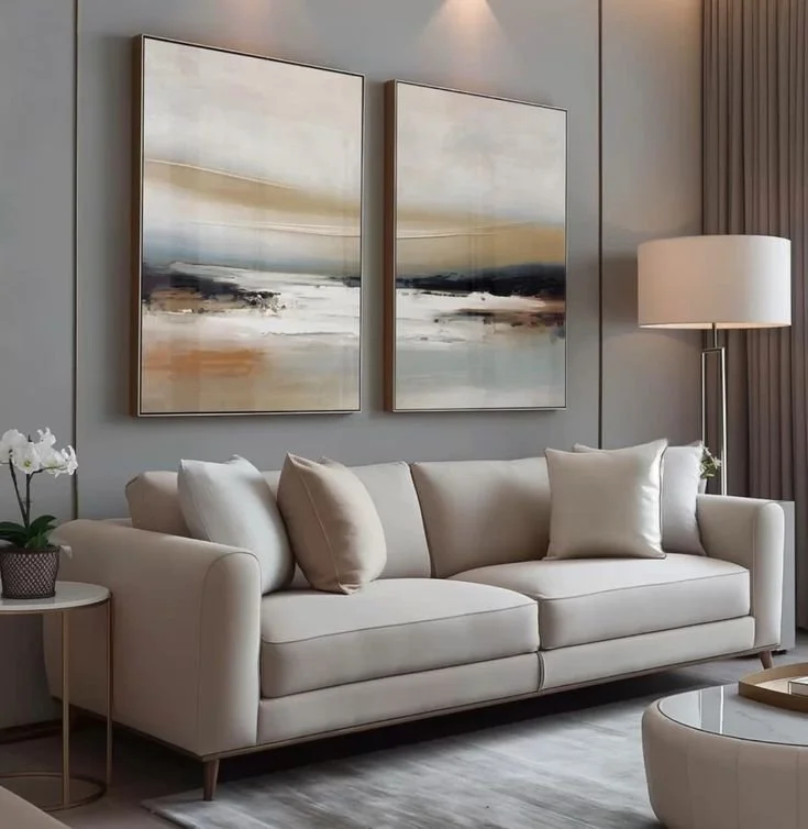 A living room with a white sofa, two abstract landscape paintings above it, a side table with a plant, a tall floor lamp, and a gray curtain on the right.