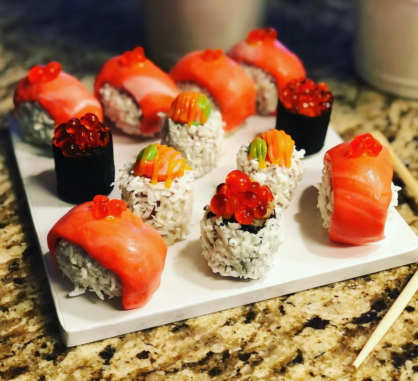 Assorted sushi rolls on a white platter, featuring salmon, rice, seaweed, and fish roe.