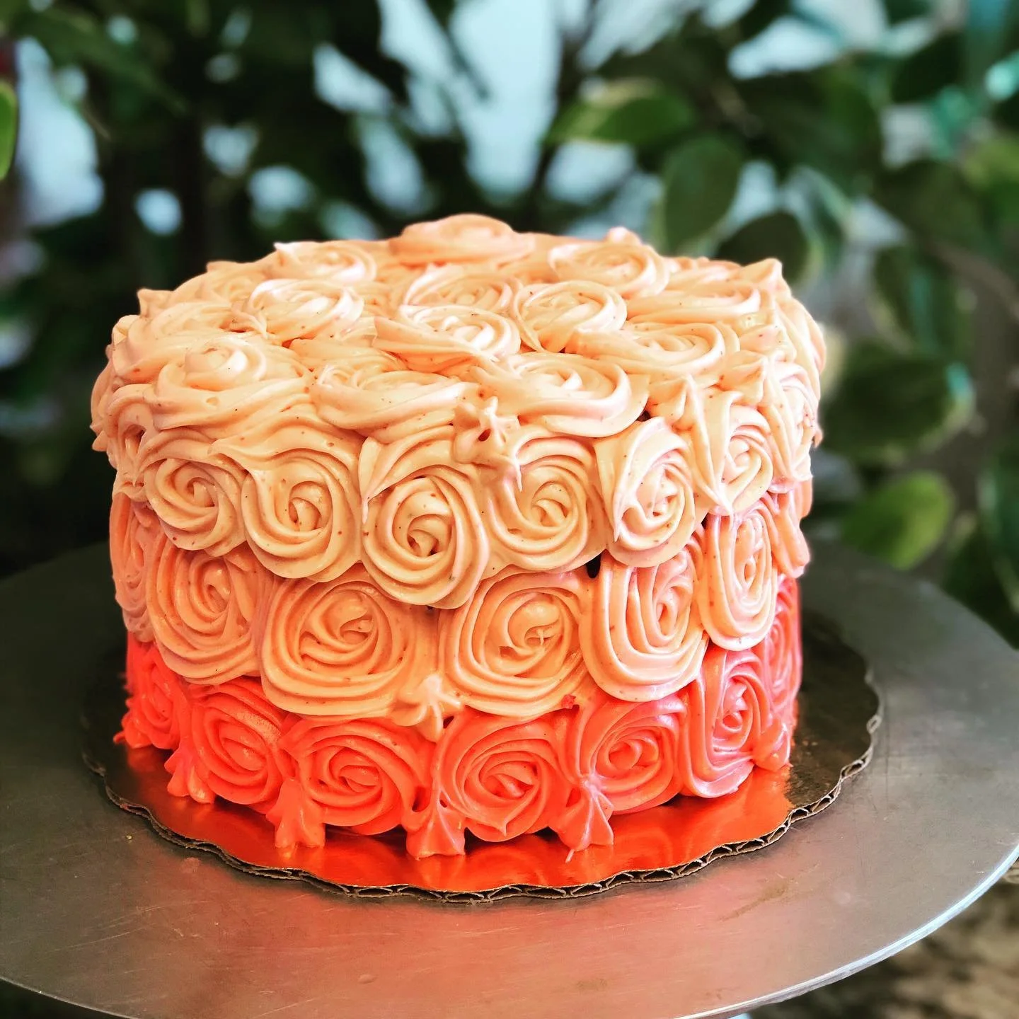 A round cake decorated with peach-colored buttercream roses, placed on a silver cake board.