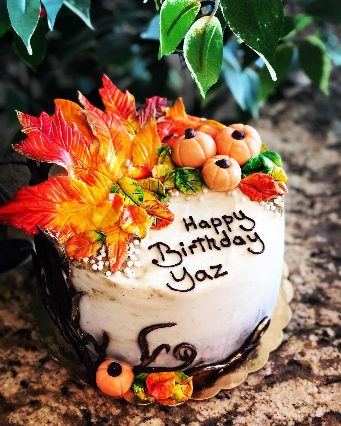 A birthday cake decorated with colorful autumn leaves and small pumpkins, with a handwritten message that reads 'Happy Birthday Yaz.'