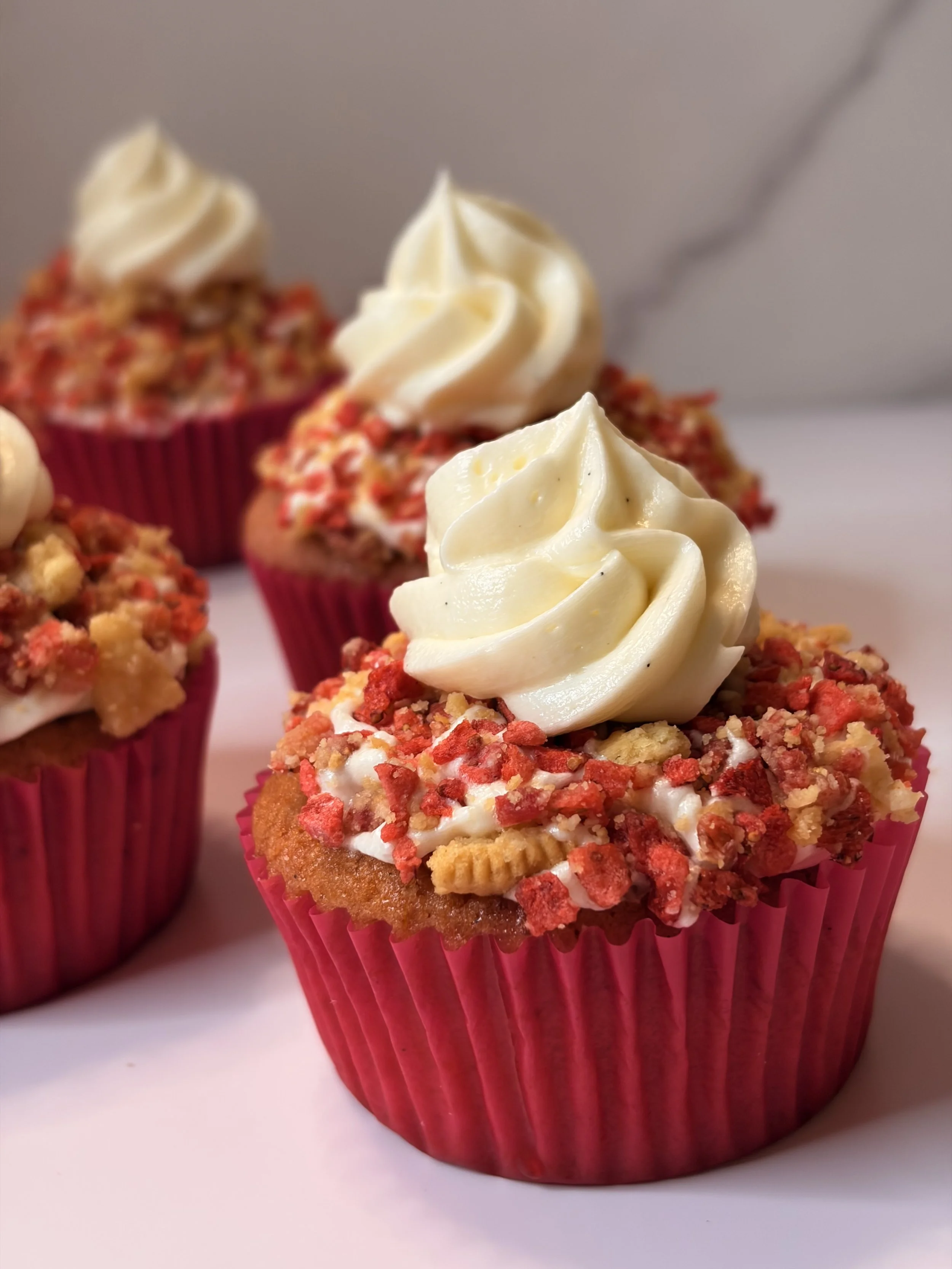 Close-up of a decorated cupcake with white frosting piped on top, in a pink cupcake liner, and sprinkled with red and yellow crumbs.