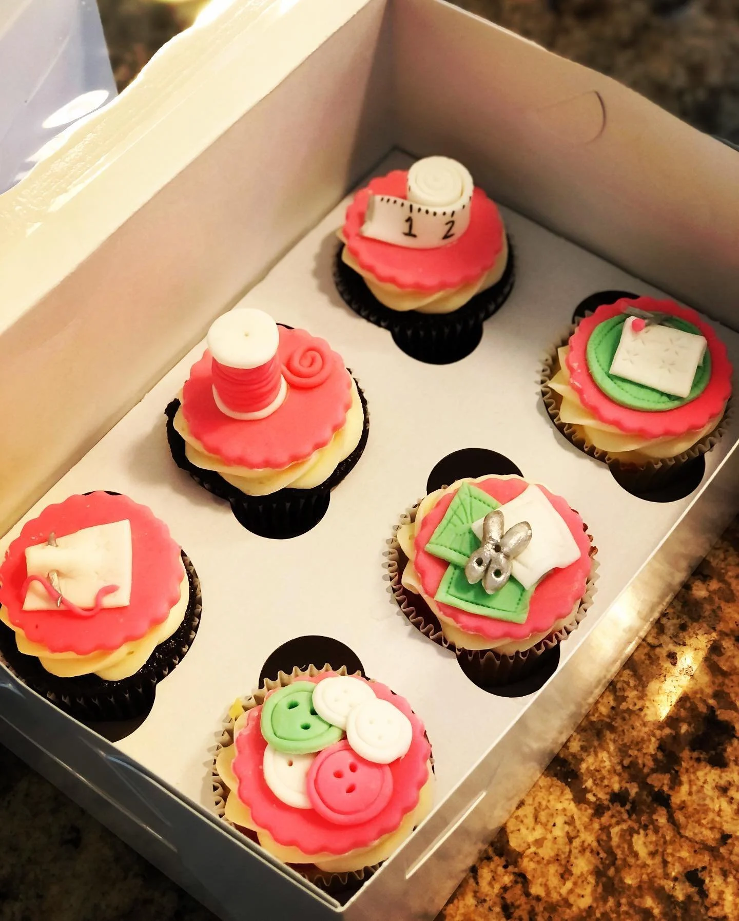 Box of decorated cupcakes with holiday and winter-themed decorations including buttons, ribbons, and small ornaments.