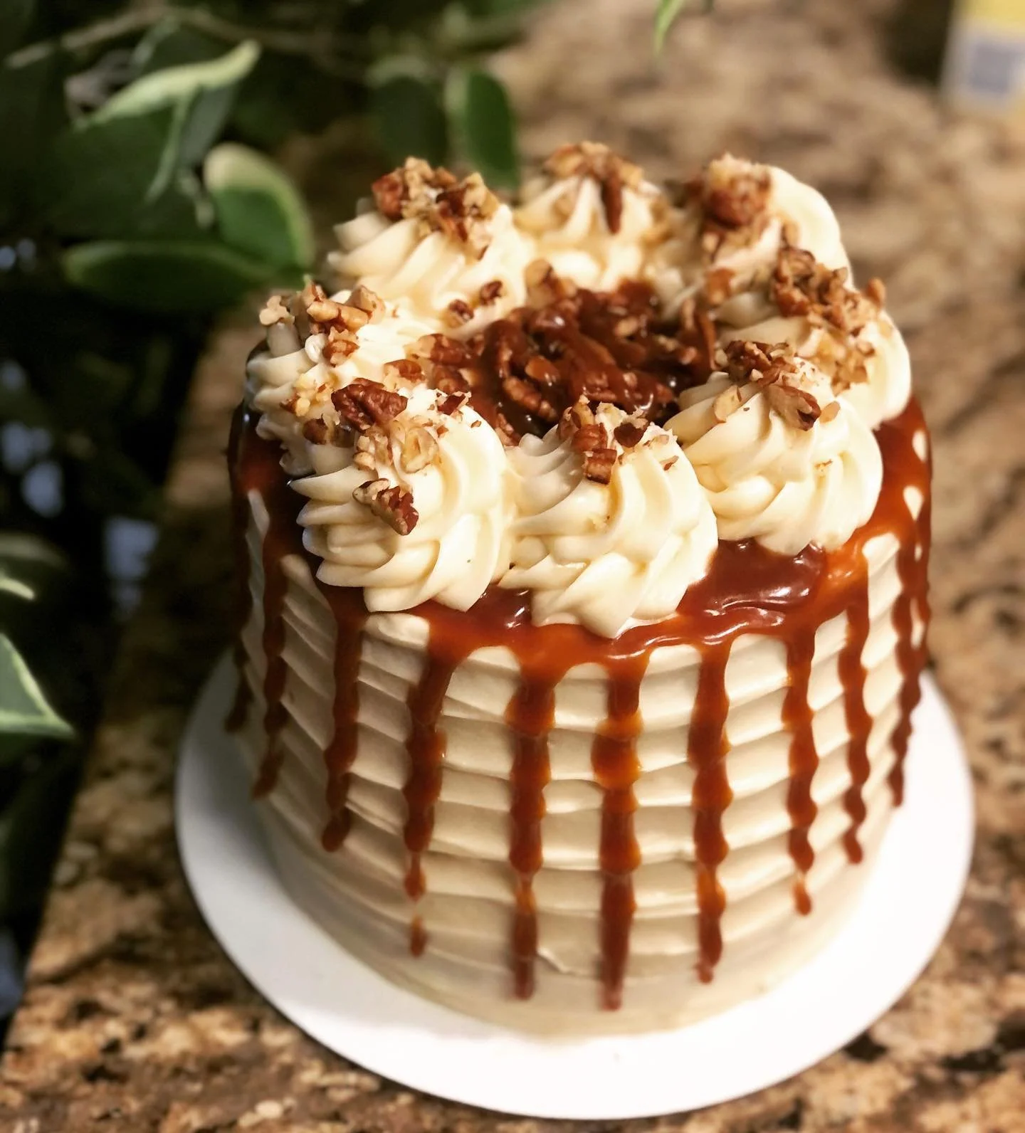 A cake decorated with swirls of white frosting, caramel drizzle on the sides, and topped with chopped nuts and caramel syrup.