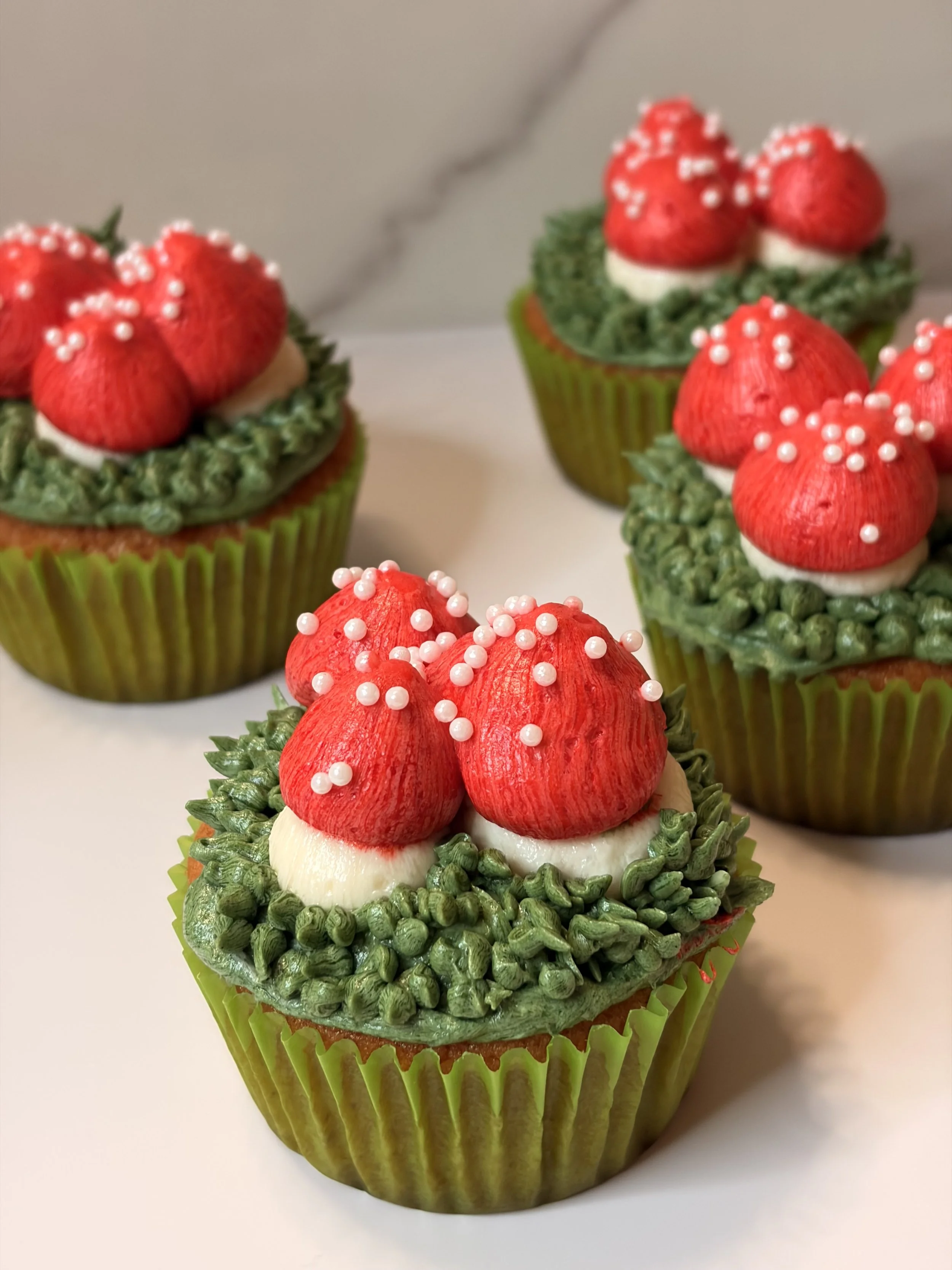 Decorative cupcakes with red mushroom-shaped toppers, green frosting, and white sprinkles, placed in green cupcake liners.