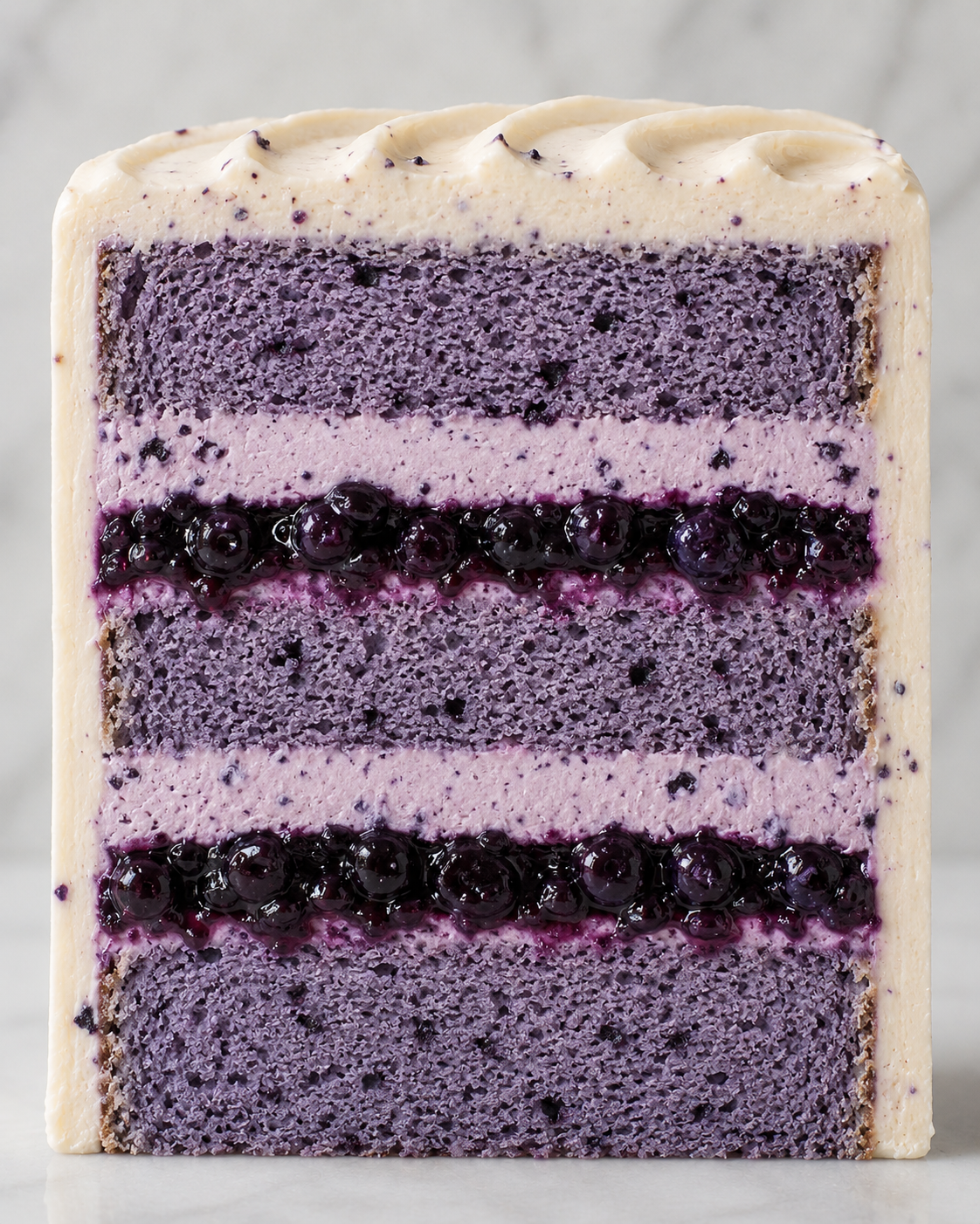 Cross-section of a layered blueberry cake with purple and white layers, blueberry filling, and cream frosting on top.