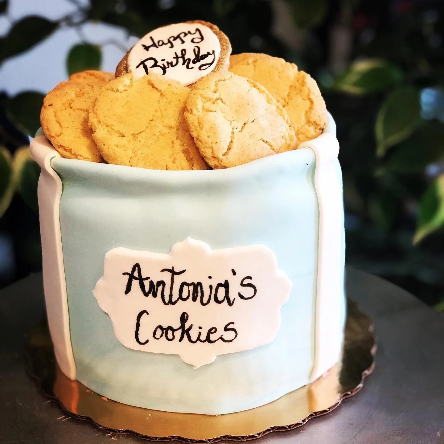 A container of homemade cookies labeled 'Antonia's Cookies' with a cookie that says 'Happy Birthday' on top.