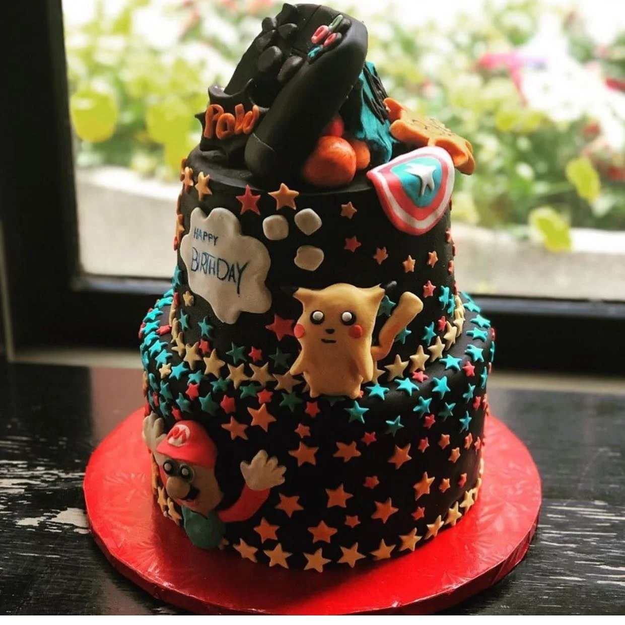 A two-tiered birthday cake decorated with Super Mario characters and themed edible decorations, with a black starry background and red cake base.