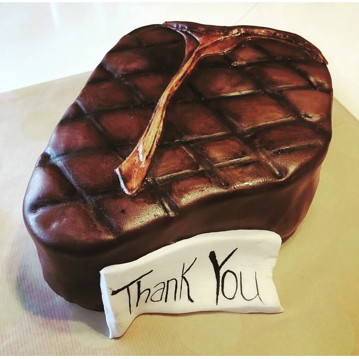 A cake decorated to look like a folded leather office chair, with a small wooden leaf on top and a white sign in front that says 'Thank You'.