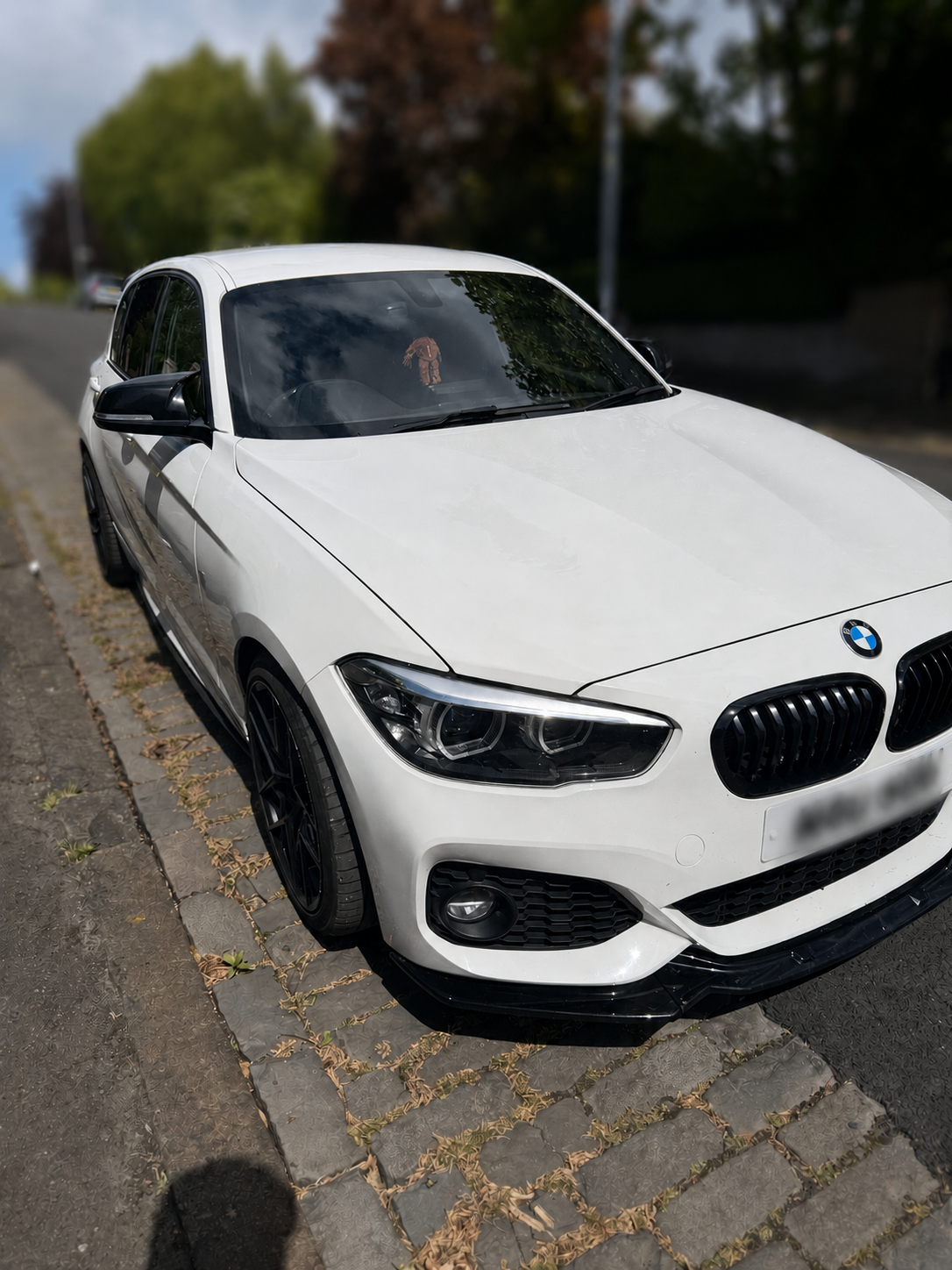 A white BMW car parked on a street with trees in the background.