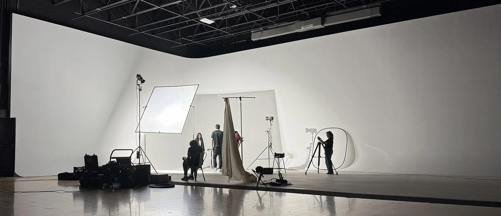 Studio with large white backdrop, lighting equipment, and crew preparing for filming or photoshoot.