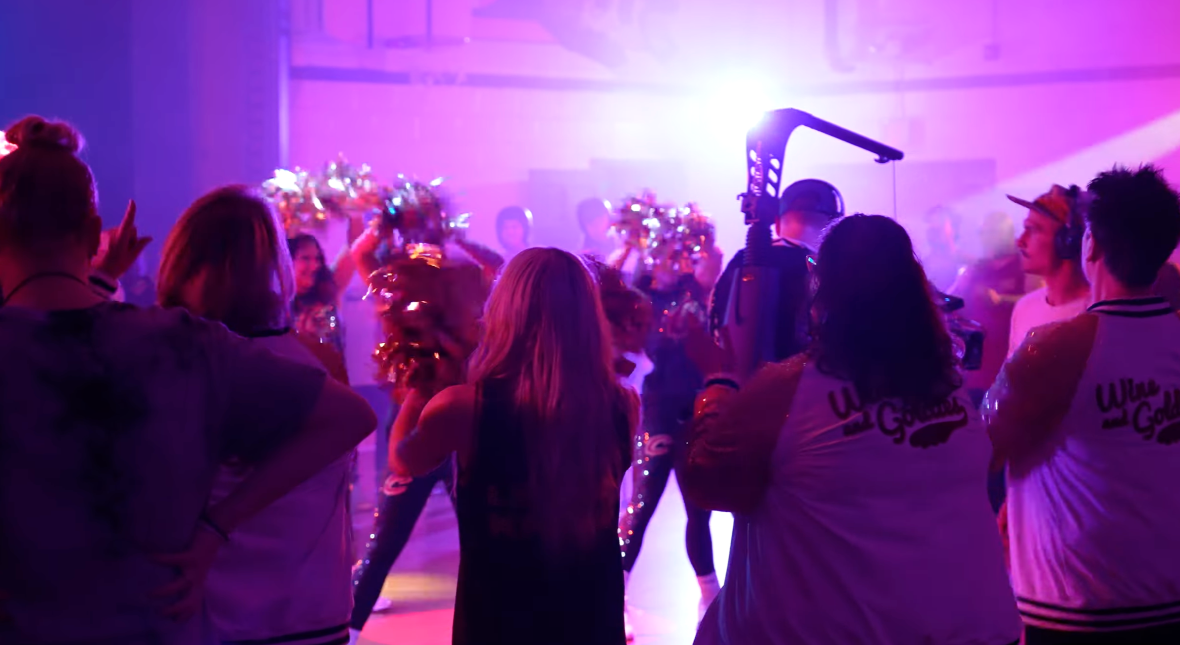 People dancing and socializing at a party with colorful purple and pink lighting.