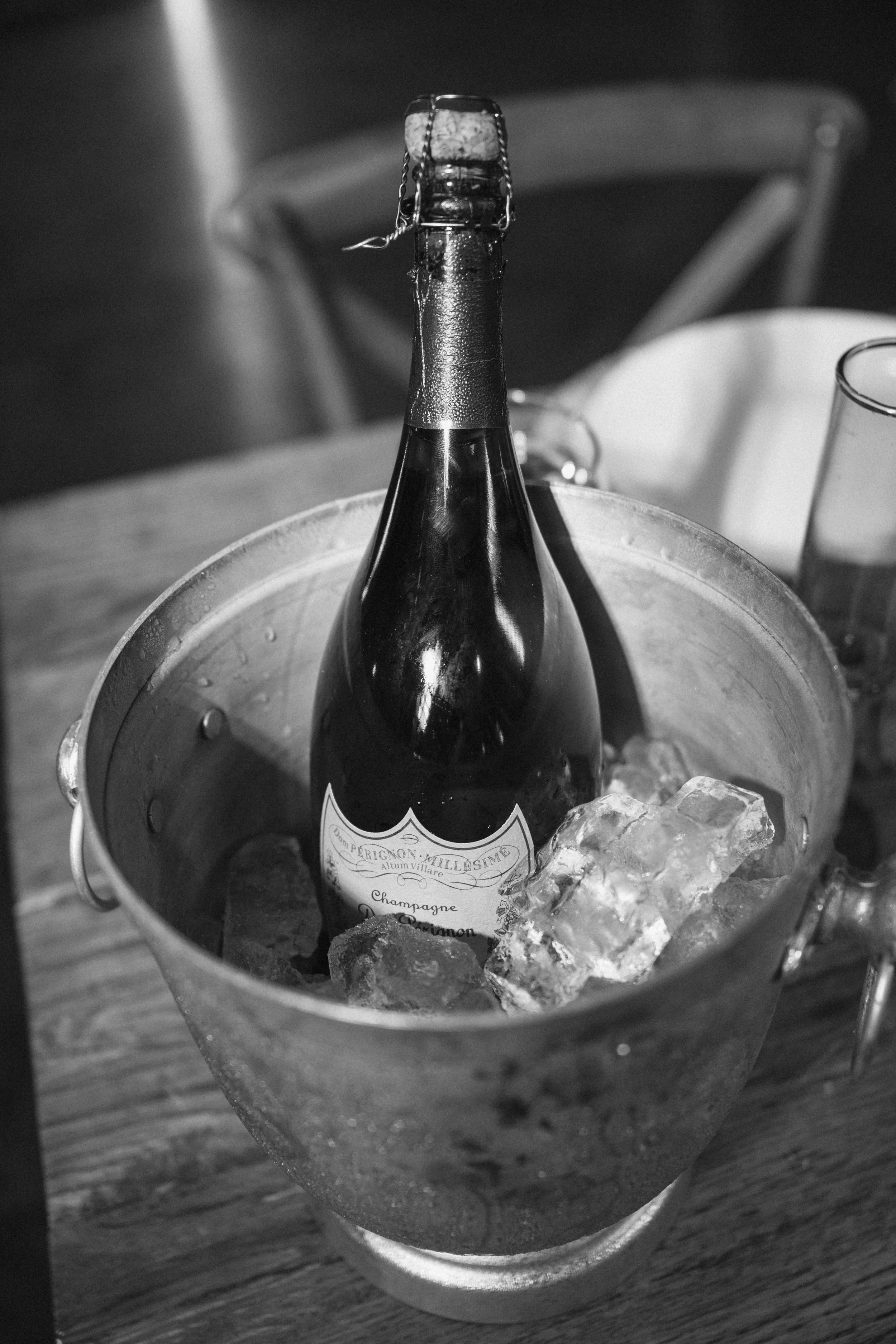 A bottle of champagne on ice in a metal bucket filled with ice cubes, placed on a wooden table.