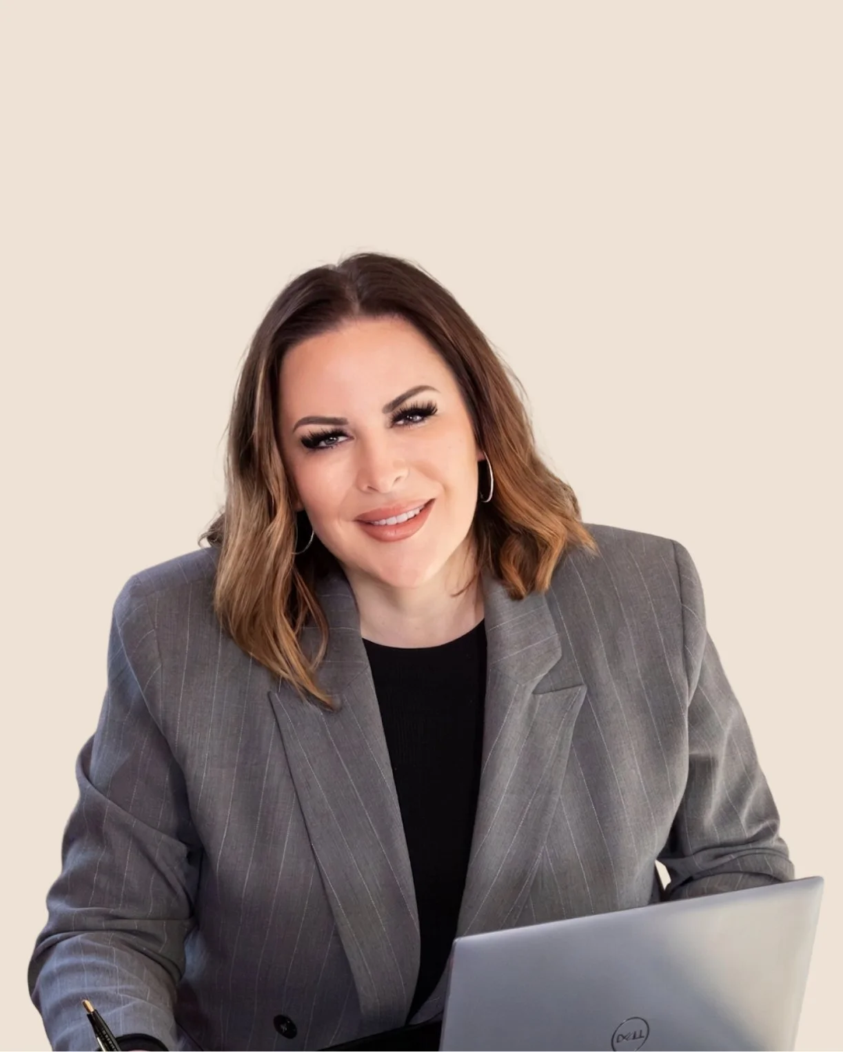 Leadership coach, keynote speaker, and author Alexandra Gerritsen is wearing a gray blazer, sitting at a desk with a silver laptop, smiling at the camera.