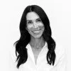 A black-and-white photograph of a smiling woman with long, dark hair wearing a collared shirt.