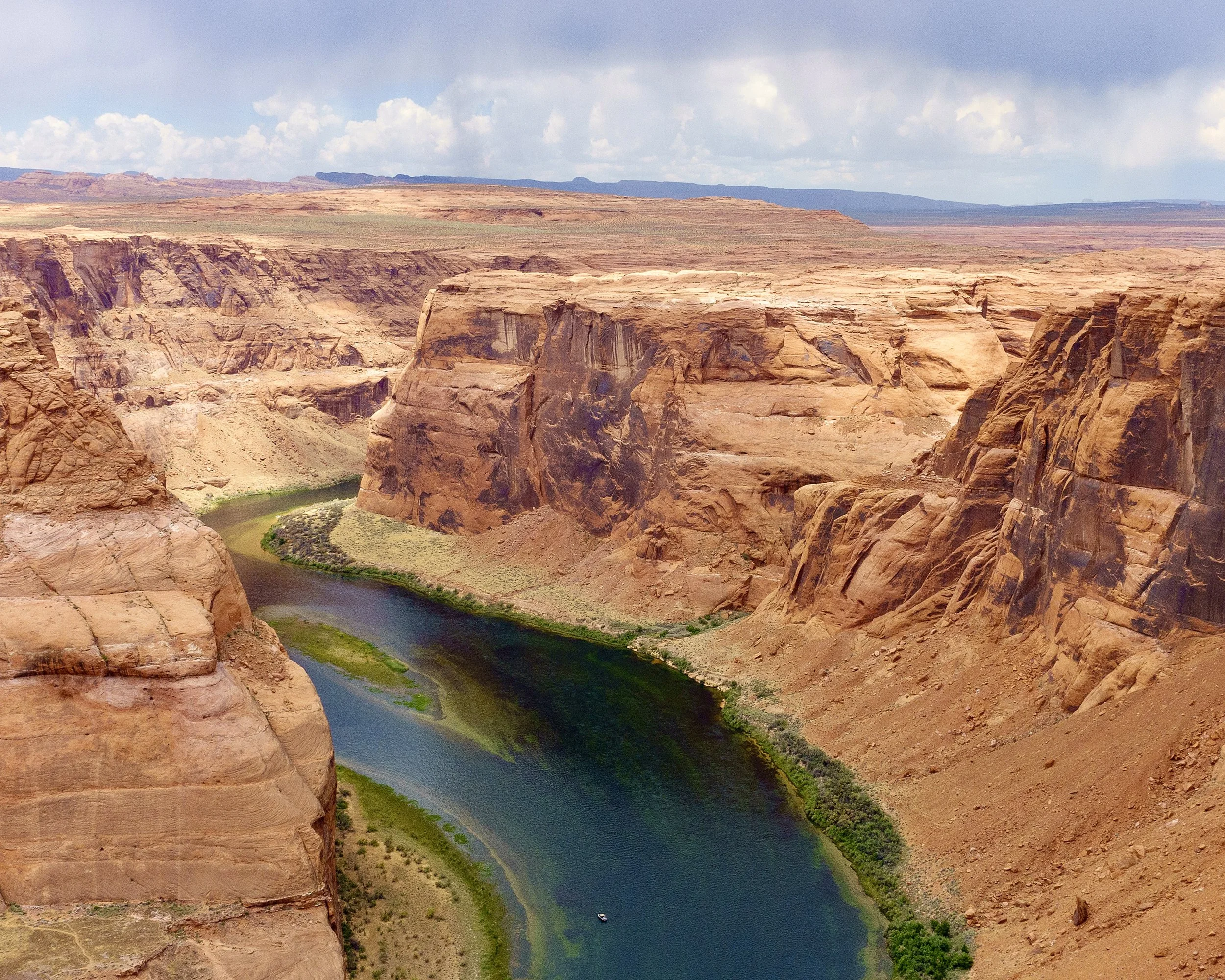 Horseshoe Bend, Arizona. A river runs through a deep canyon with rugged, reddish rock walls, under a partly cloudy sky.
