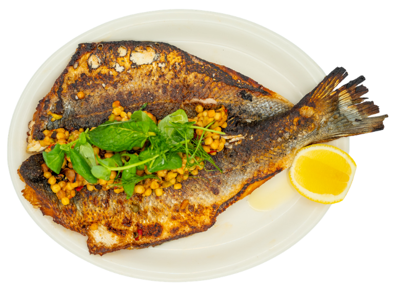 Whole grilled fish garnished with herbs and a lemon wedge on a white plate.