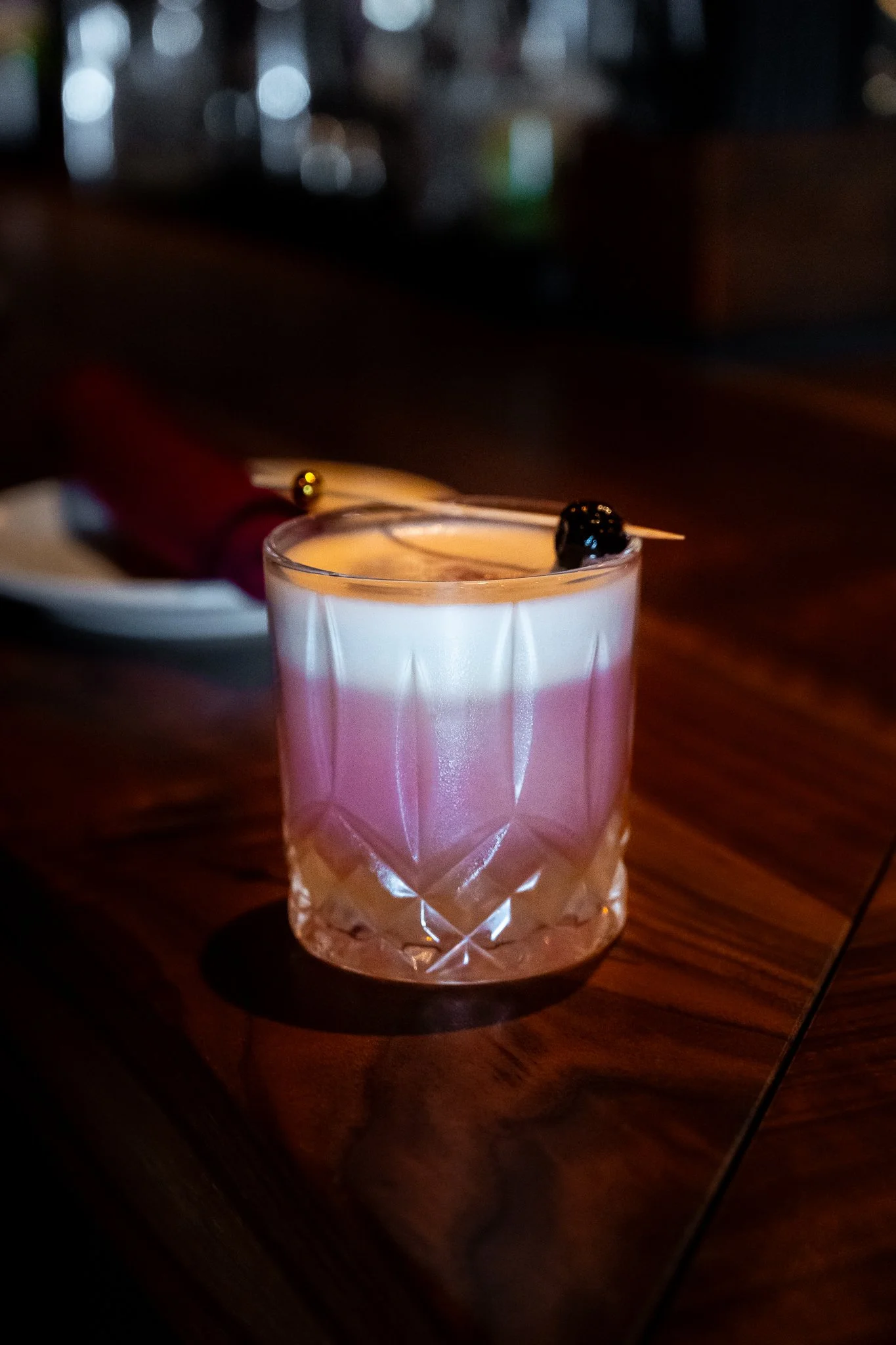 A pink candle in a glass holder with a gold and black decorative topper on top of the candle, placed on a wooden surface.
