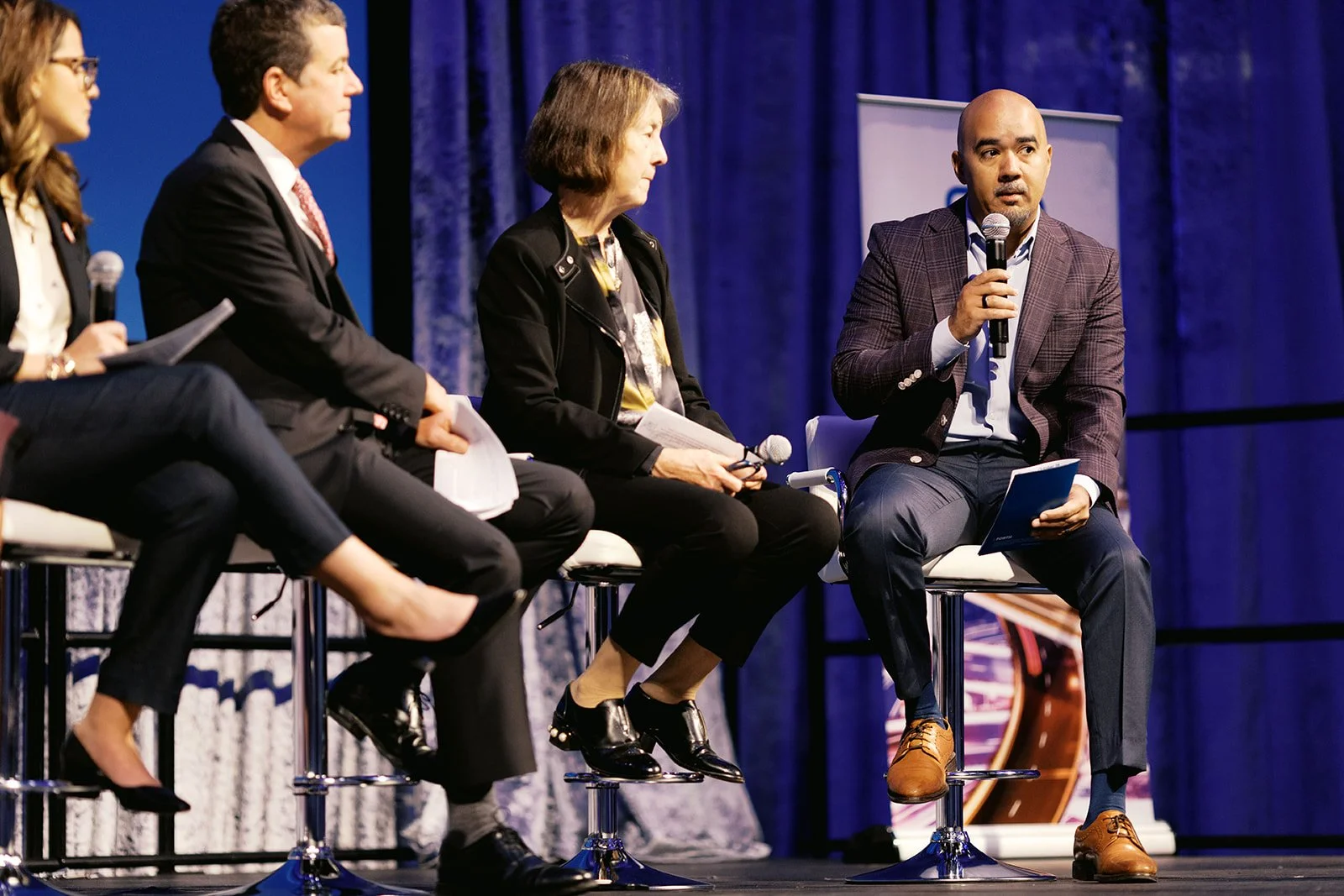 4 seated people talking on a stage, one with a microphone.