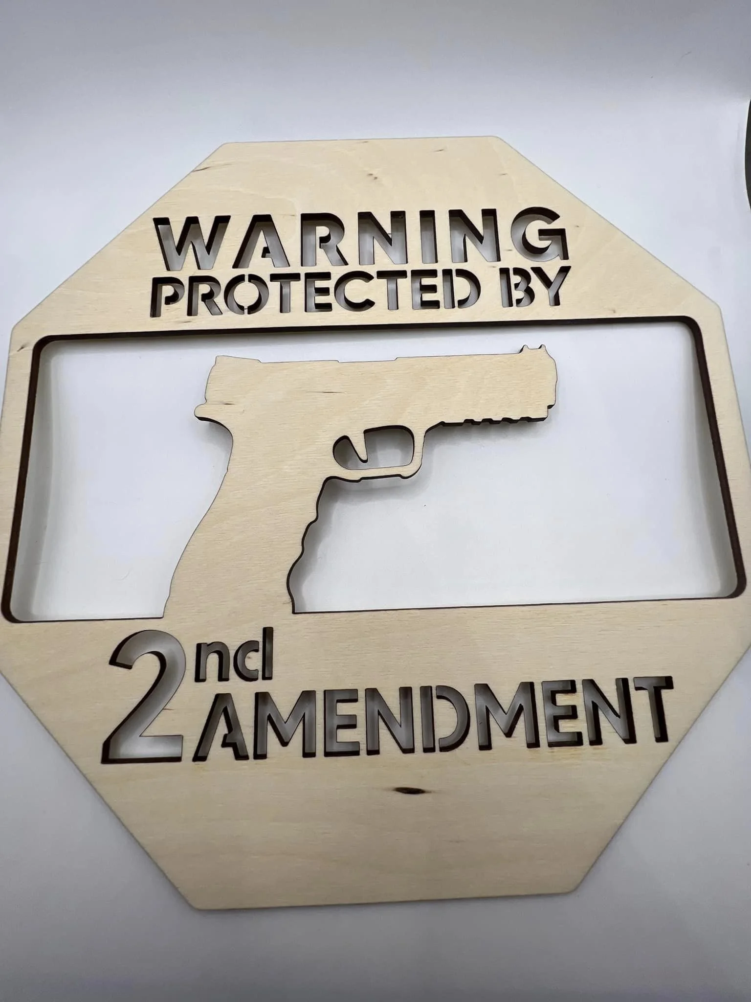 Wooden sign with cutout of a handgun and text that reads, 'Warning Protected by 2nd Amendment.'