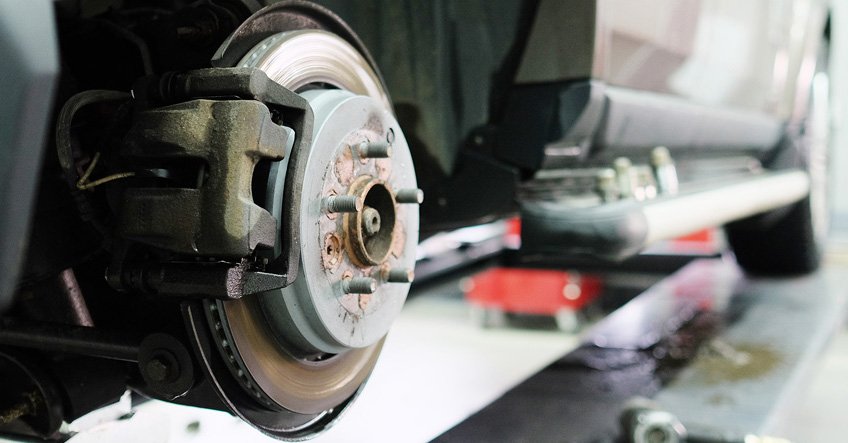 Close-up of a car's brake disc and caliper assembly, with the wheel removed, in the Walnut Creek Brake and Tire garage.