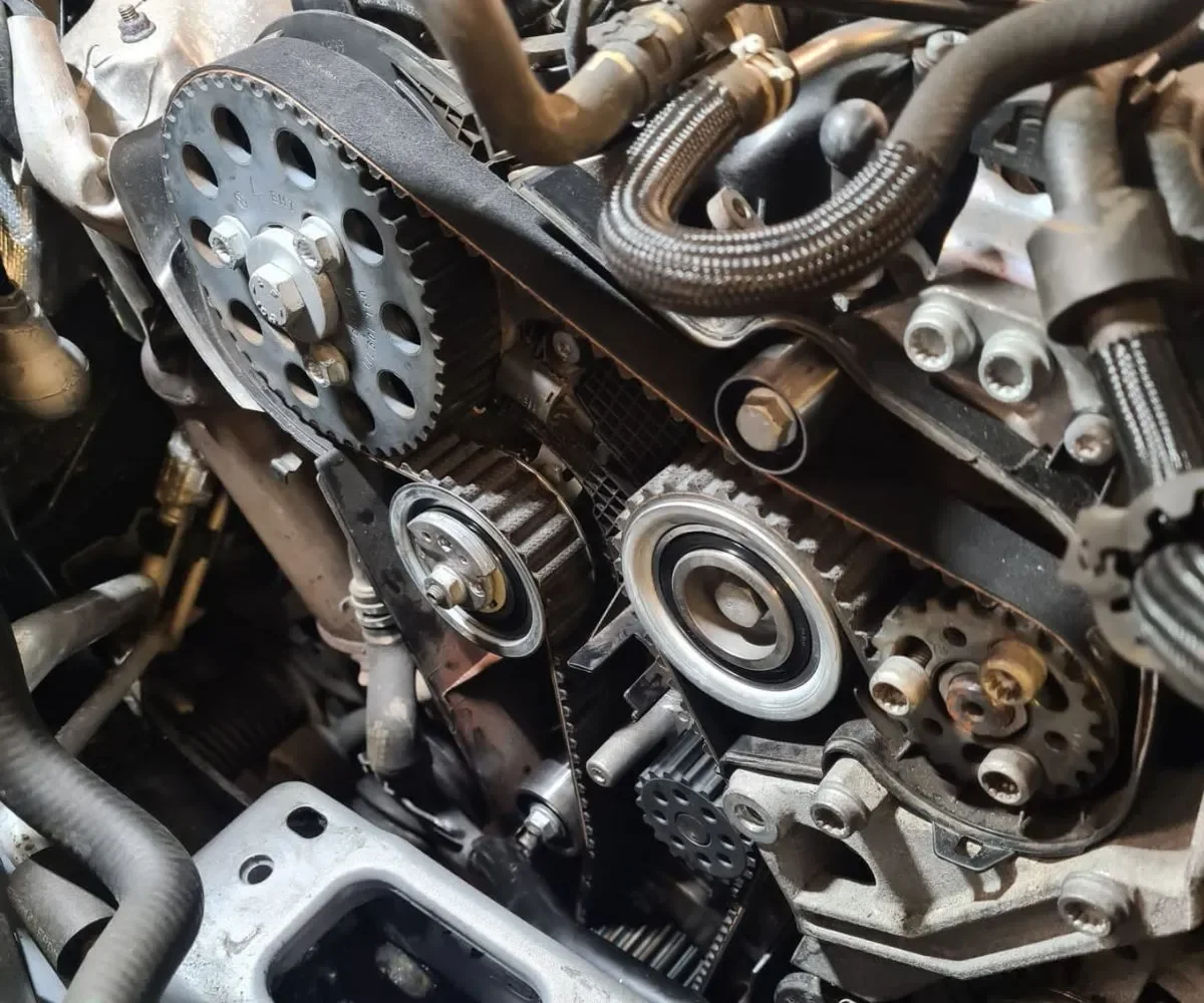 Close-up view of an engine's timing belt and gears, showing the belt wrapped around pulleys and tensioners.