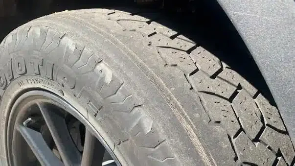 Close-up of a car tire and rim, showing worn tire tread pattern on the tire