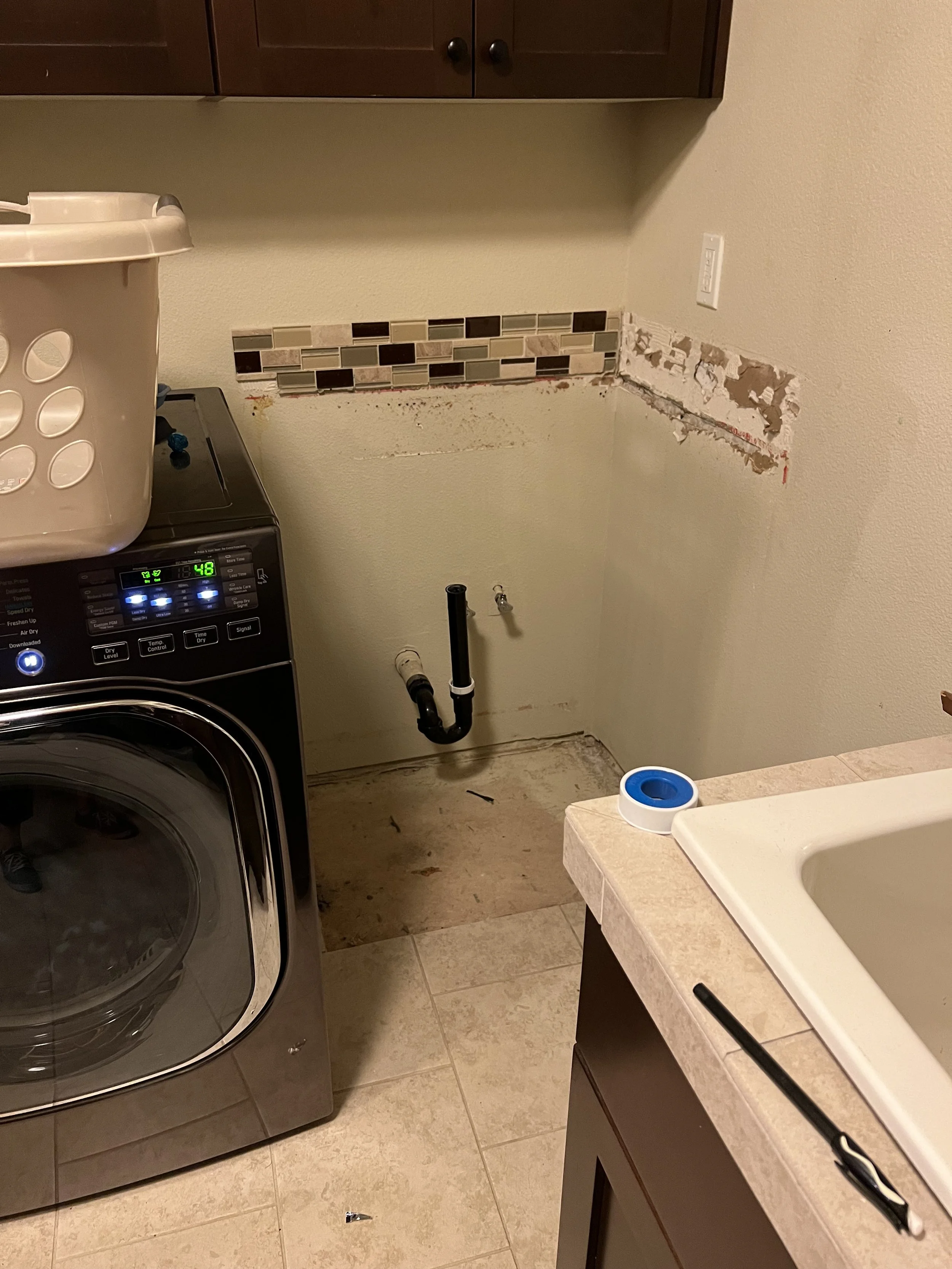 Before renovation: a laundry room mid-demo, with a washer and dryer and a wall stripped down to patches.